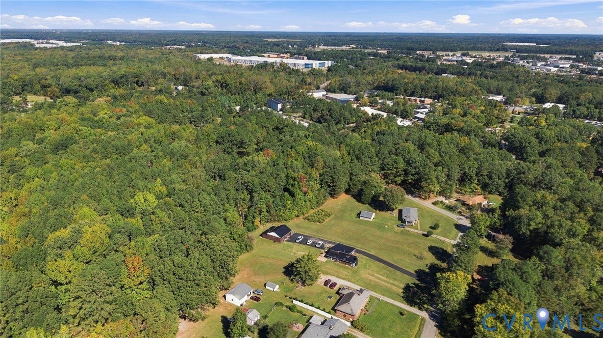 Aerial perspective featuring expansive forested acreage, multiple cleared grass parcels, and paved driveway access