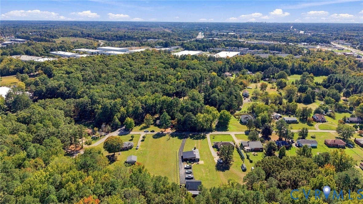 Aerial perspective showcasing a spacious lot featuring mature trees, expansive open green space, and paved driveway access