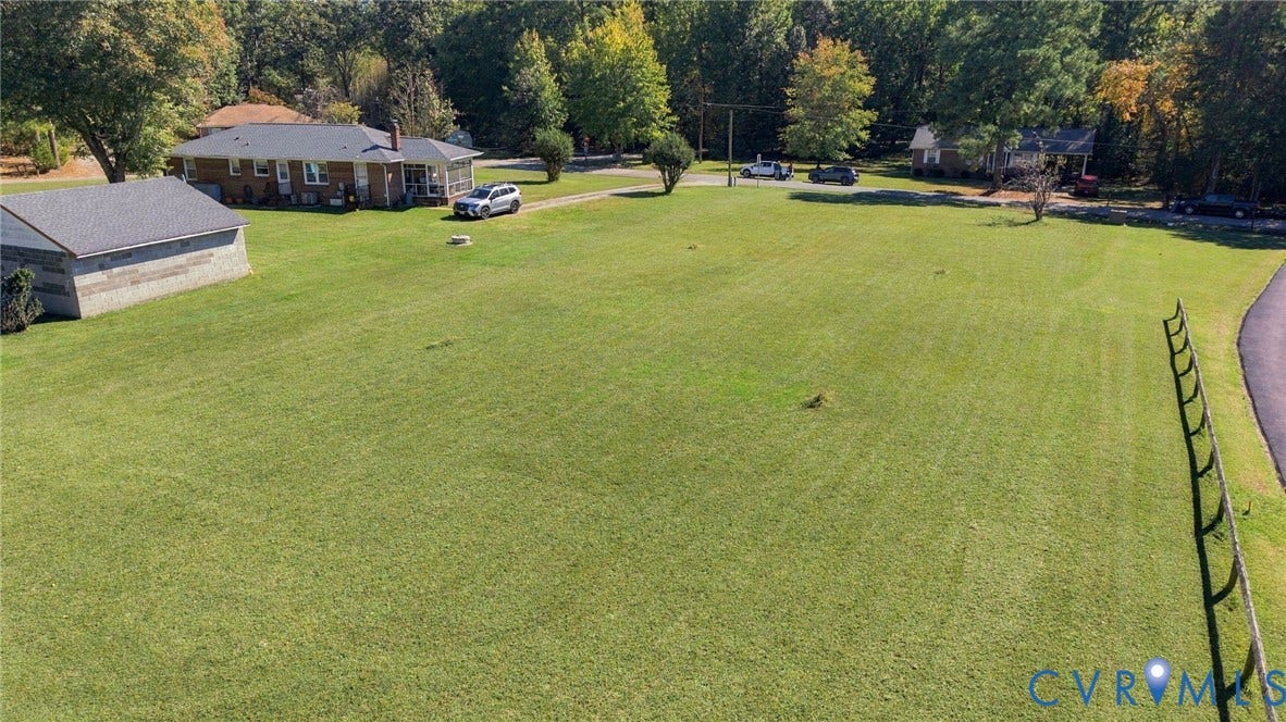 Expansive parcel featuring a manicured lawn, detached structure with a pitched roof, asphalt driveway, and perimeter fencing