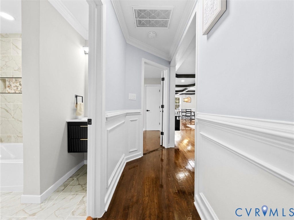 1811 Murdoch Road, Henrico, VA 23229 Hallway featuring crown molding, wainscoting, and wood-finish flooring, complemented by a black floating vanity and tiled tub surround