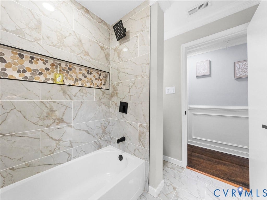 1811 Murdoch Road, Henrico, VA 23229 Shower enclosure with large-format tile walls, recessed pebble-stone accent niche, matte black fixtures, and built-in tub