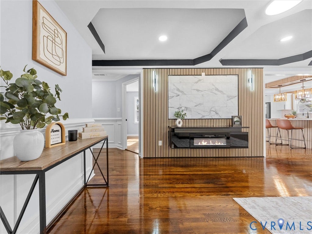 1811 Murdoch Road, Henrico, VA 23229 Wood-finish flooring, tray ceilings with contrasting trim, and a floor-to-ceiling vertical slat accent wall featuring a stone-style panel and built-in electric fireplace