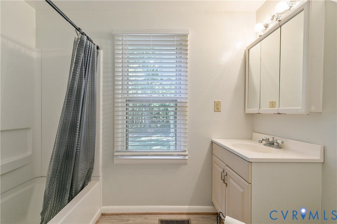 20311 McKenney Highway, Dinwiddie, VA 23882 Bathroom featuring a white vanity cabinet with an integrated sink, a three-door mirrored medicine cabinet, a light-toned wood-finish floor, and a white tub-shower combination with horizontal blinds