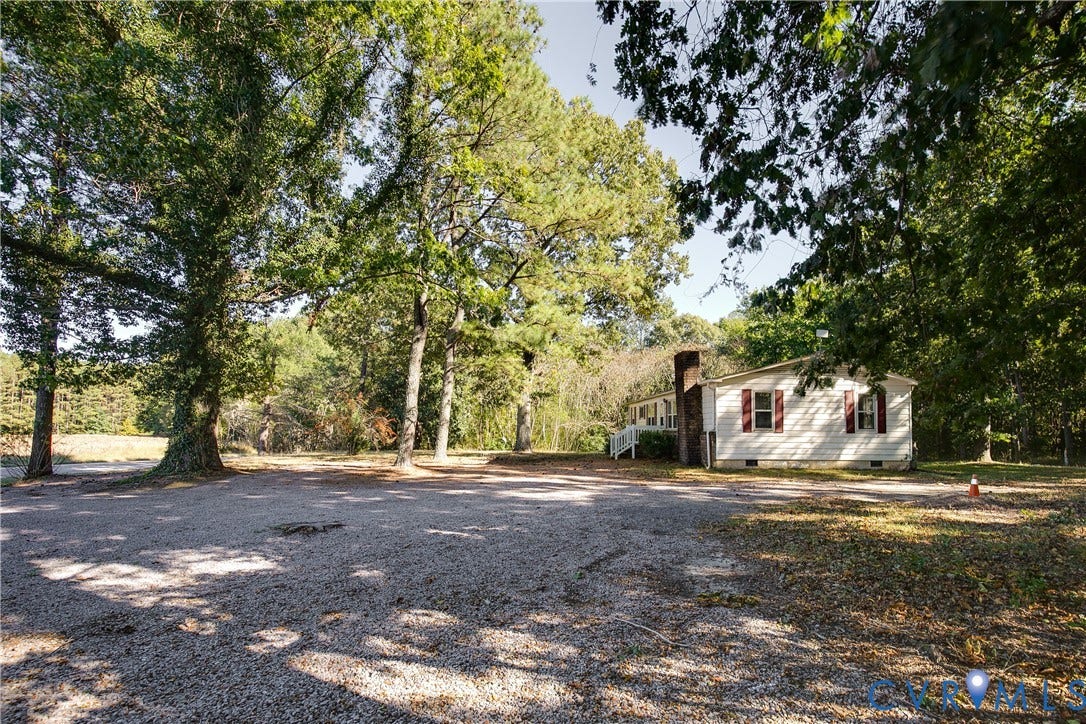 20311 McKenney Highway, Dinwiddie, VA 23882 Exterior featuring light-colored horizontal siding, red shutters, a brick chimney, and a gravel lot surrounded by mature trees
