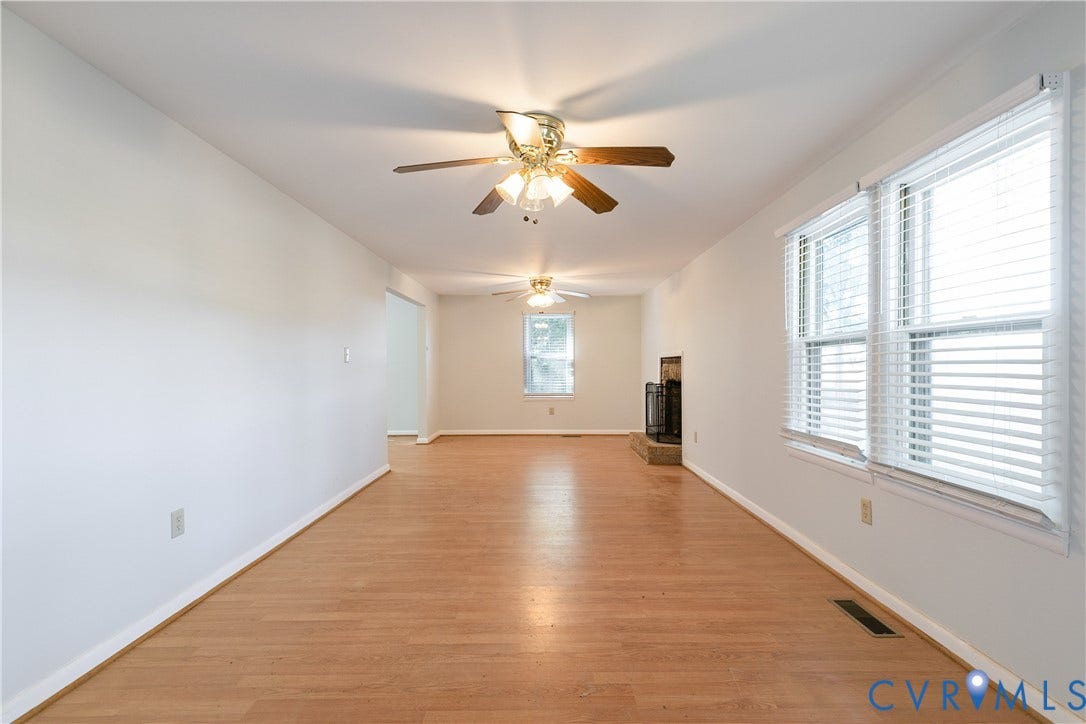 20311 McKenney Highway, Dinwiddie, VA 23882 Living area featuring wood-finish flooring, two ceiling fans, large windows with horizontal blinds, and a fireplace with a stone-finish hearth