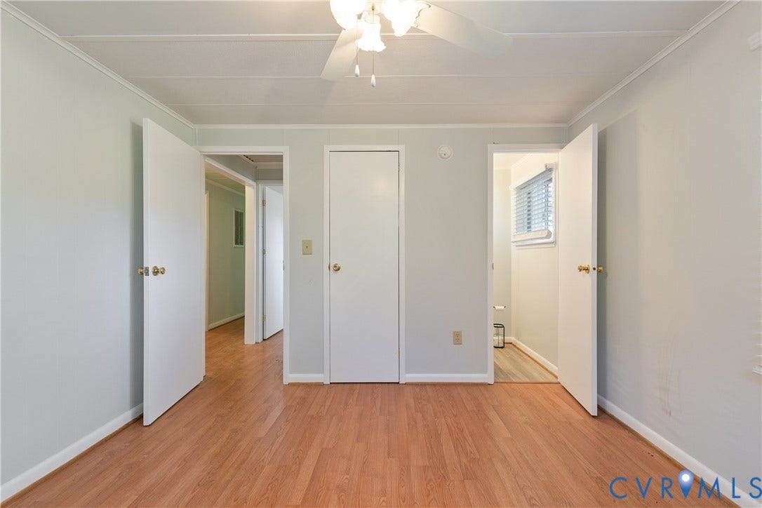 20311 McKenney Highway, Dinwiddie, VA 23882 Interior space featuring wood-finish flooring, neutral wall paint, three white interior doors, and a ceiling-mounted fan with light fixture