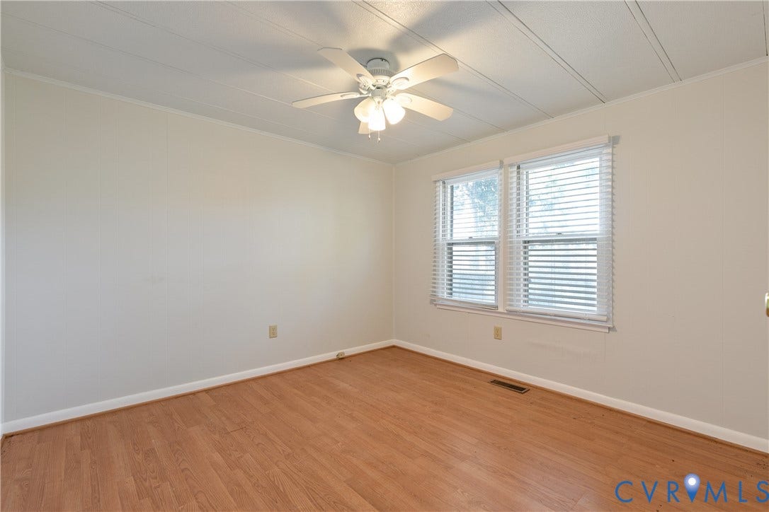 20311 McKenney Highway, Dinwiddie, VA 23882 Neutral-toned interior space featuring wood-finish flooring, white wall paneling, a multi-blade ceiling fan with integrated lighting, and dual windows equipped with horizontal blinds