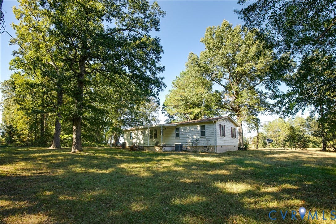 20311 McKenney Highway, Dinwiddie, VA 23882 Single-story residence featuring light-colored horizontal siding, a covered front porch, and shutters, situated on a lot with expansive grass and mature trees