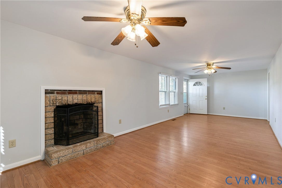 20311 McKenney Highway, Dinwiddie, VA 23882 Interior space featuring wood-finish flooring, two ceiling fans with integrated lighting, and a brick fireplace with a raised hearth