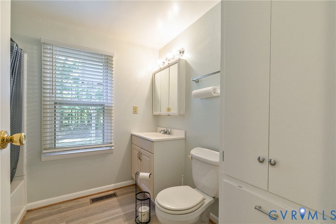20311 McKenney Highway, Dinwiddie, VA 23882 Bathroom featuring wood-finish flooring, a white vanity with integrated sink, a mirrored medicine cabinet, a full-height built-in storage cabinet, and a window with horizontal blinds