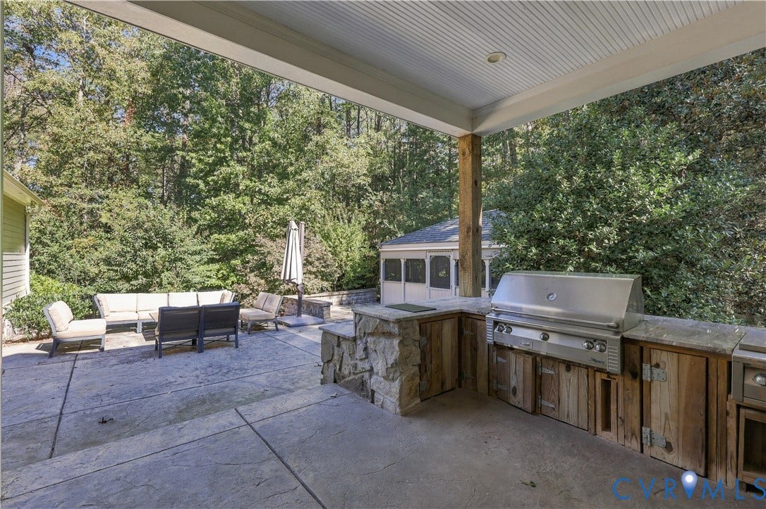 3056 Greywalls Drive, Powhatan, VA 23139 Covered patio featuring a built-in outdoor kitchen with stone masonry, wood-finish cabinetry, a stainless steel grill, and a concrete paver surface