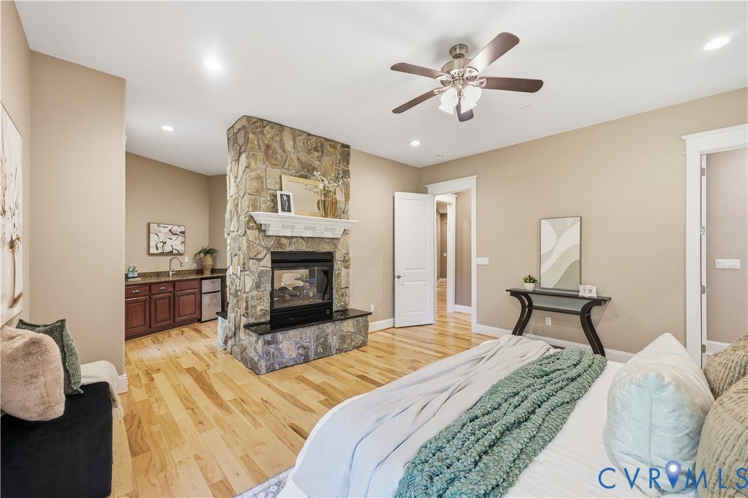 3056 Greywalls Drive, Powhatan, VA 23139 Stone-faced double-sided fireplace with a raised hearth, wood-finish flooring, recessed lighting, ceiling fan, and built-in wet bar featuring dark wood cabinetry and a sink