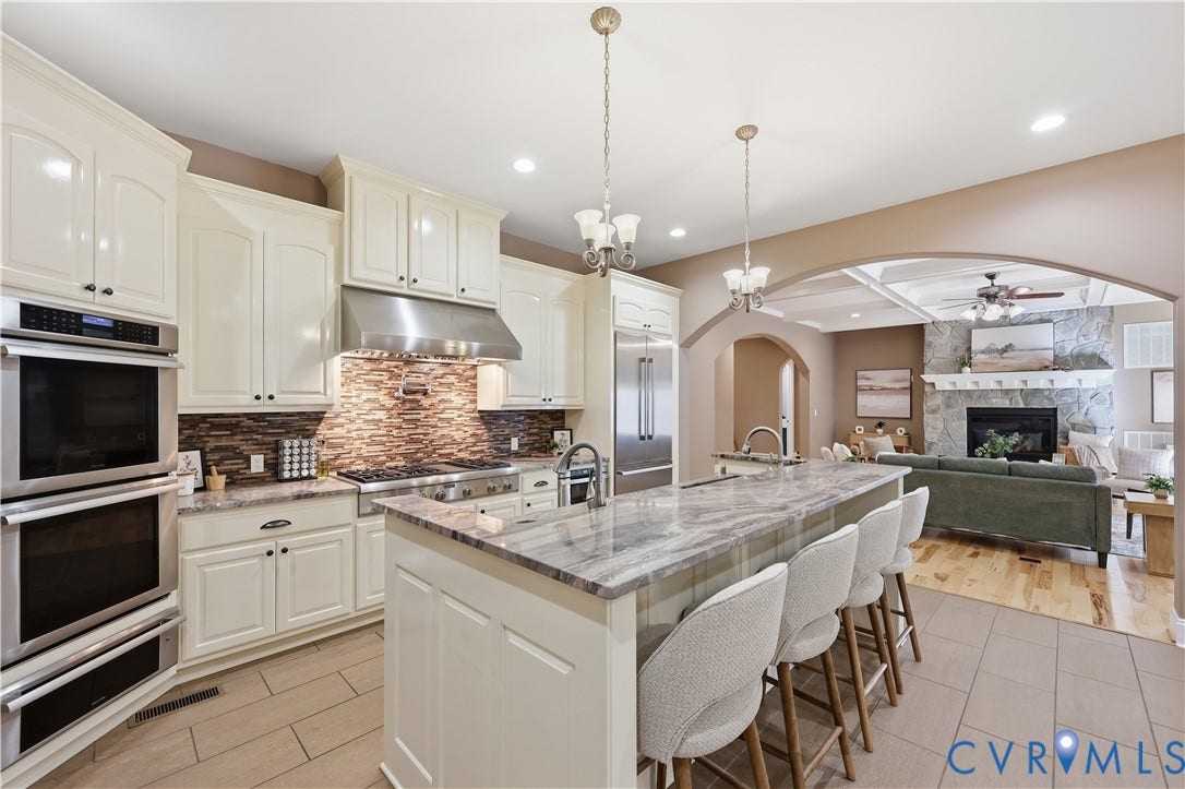 3056 Greywalls Drive, Powhatan, VA 23139 Kitchen featuring off-white cabinetry, stone-finish countertops, stainless steel appliances, a textured tile backsplash, and a central island with a prep sink