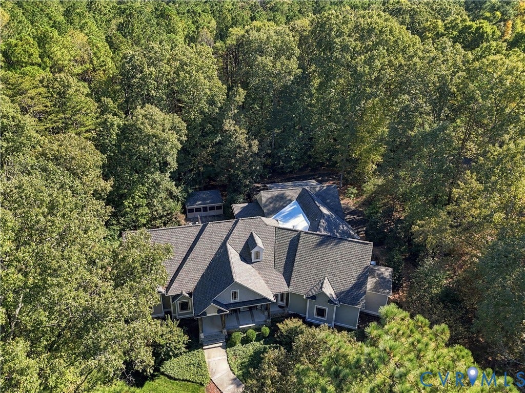 3056 Greywalls Drive, Powhatan, VA 23139 Aerial perspective of a multi-gabled residence featuring shingle roofing, exterior siding, a concrete walkway, and a detached structure, all situated on a heavily wooded lot