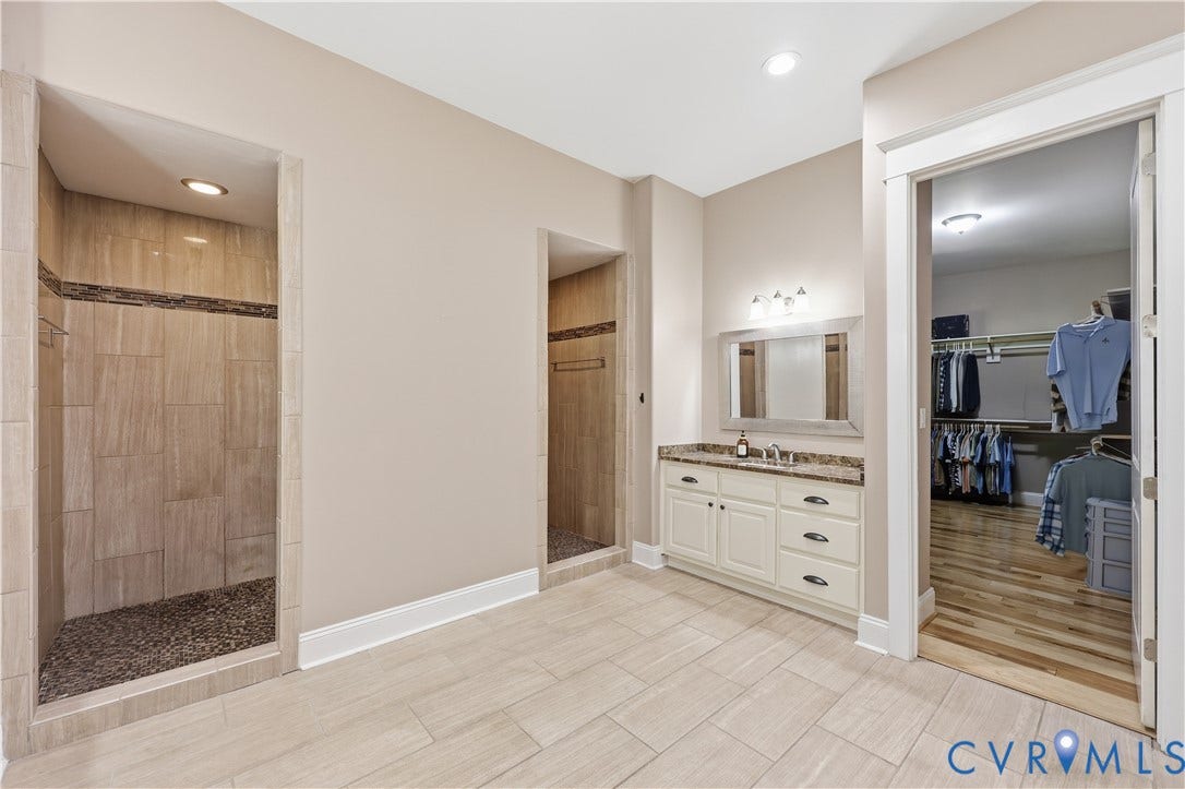 3056 Greywalls Drive, Powhatan, VA 23139 Primary Bathroom 2. Dual walk-in shower with pebble tile flooring and large-format wall tile, vanity with stone-look countertop, and walk-in closet with wood-finish flooring