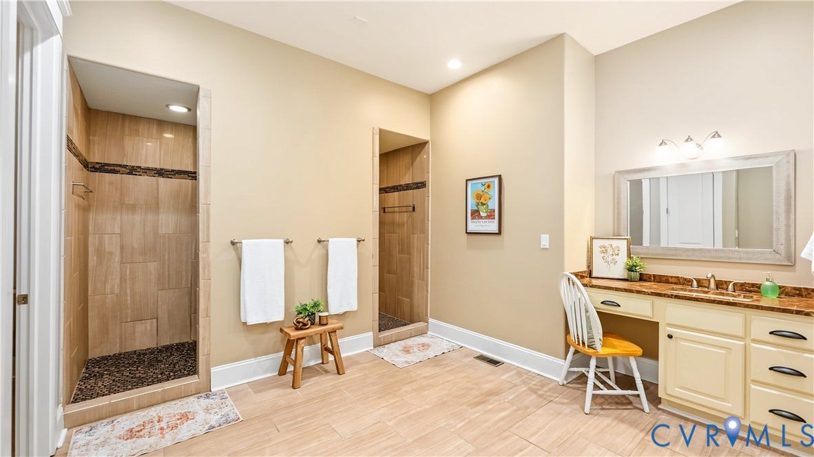 3056 Greywalls Drive, Powhatan, VA 23139 Dual walk-in shower stalls featuring stone-tile surround and pebble-texture flooring, integrated vanity with a stone countertop, and three-light wall-mounted fixture
