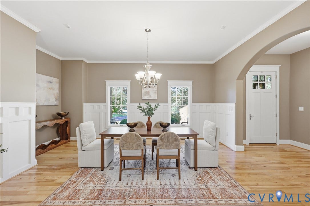 3056 Greywalls Drive, Powhatan, VA 23139 Dining area featuring wood-finish flooring, white wainscoting, a multi-arm chandelier, dual windows with decorative casing, and an arched entryway