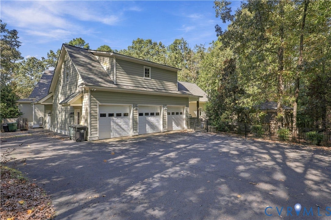 3056 Greywalls Drive, Powhatan, VA 23139 Three-car garage with white paneled doors, light green lap siding, asphalt driveway, and mature surrounding woodland