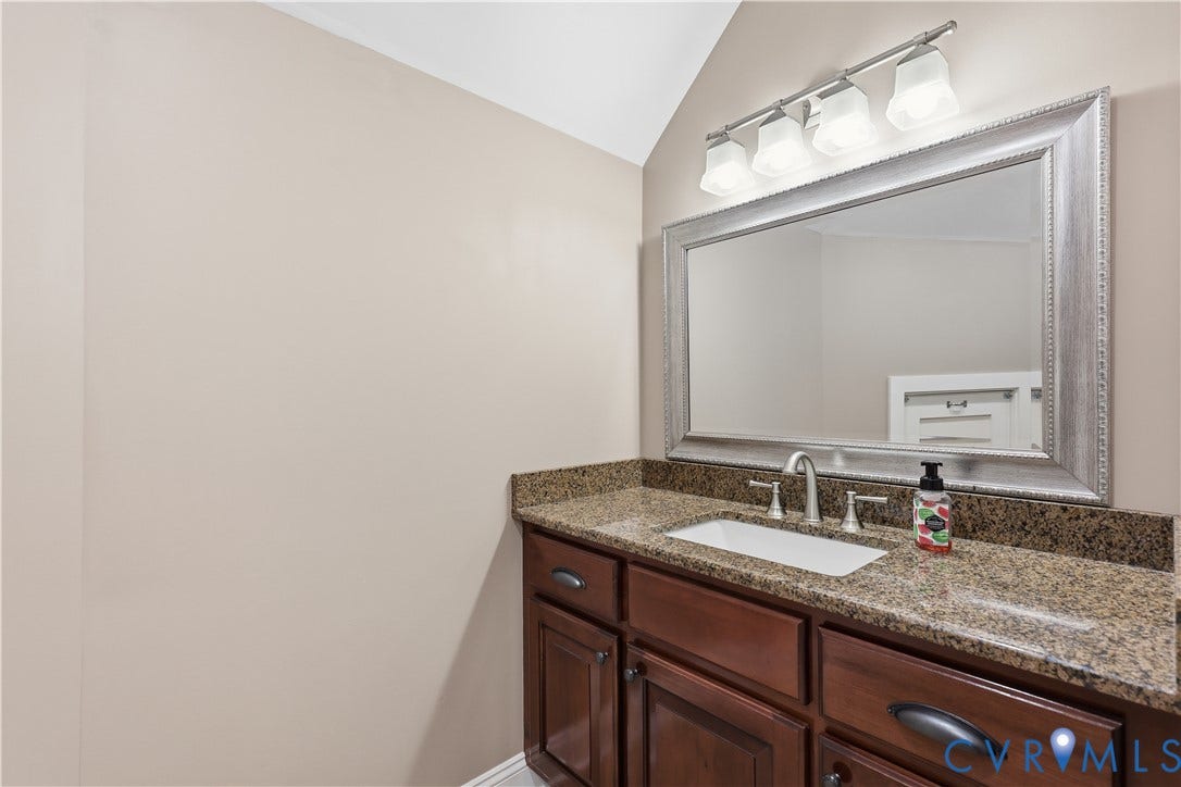 3056 Greywalls Drive, Powhatan, VA 23139 Upstairs Full Bathroom Vanity featuring dark wood cabinetry, a stone countertop with an integrated rectangular sink, a wide-framed wall mirror, and a four-light fixture