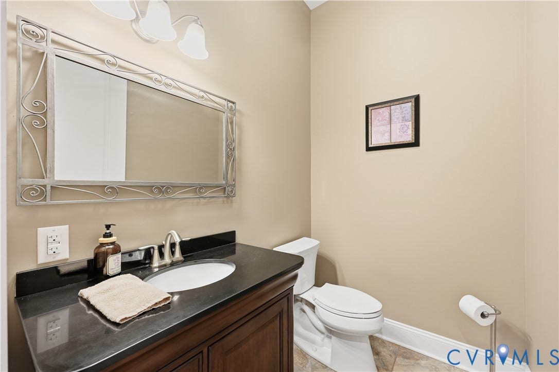 3056 Greywalls Drive, Powhatan, VA 23139 1st Floor Half Bathroom Dark stone-surfaced vanity with an integrated oval basin, decorative metallic-framed wall mirror, three-light overhead fixture, and tile flooring