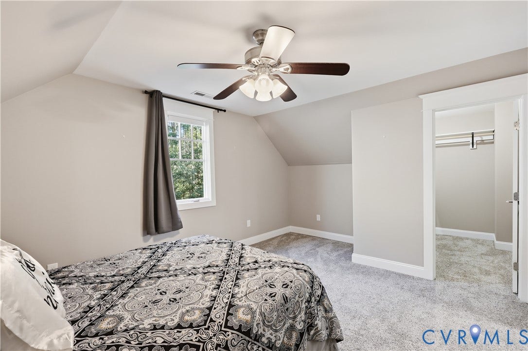 3056 Greywalls Drive, Powhatan, VA 23139 Upstairs Bedroom. Neutral wall palette featuring an angled ceiling, wall-to-wall carpeting, a multi-blade ceiling fan with integrated lighting, a multi-pane window, and a walk-in closet with built-in shelving