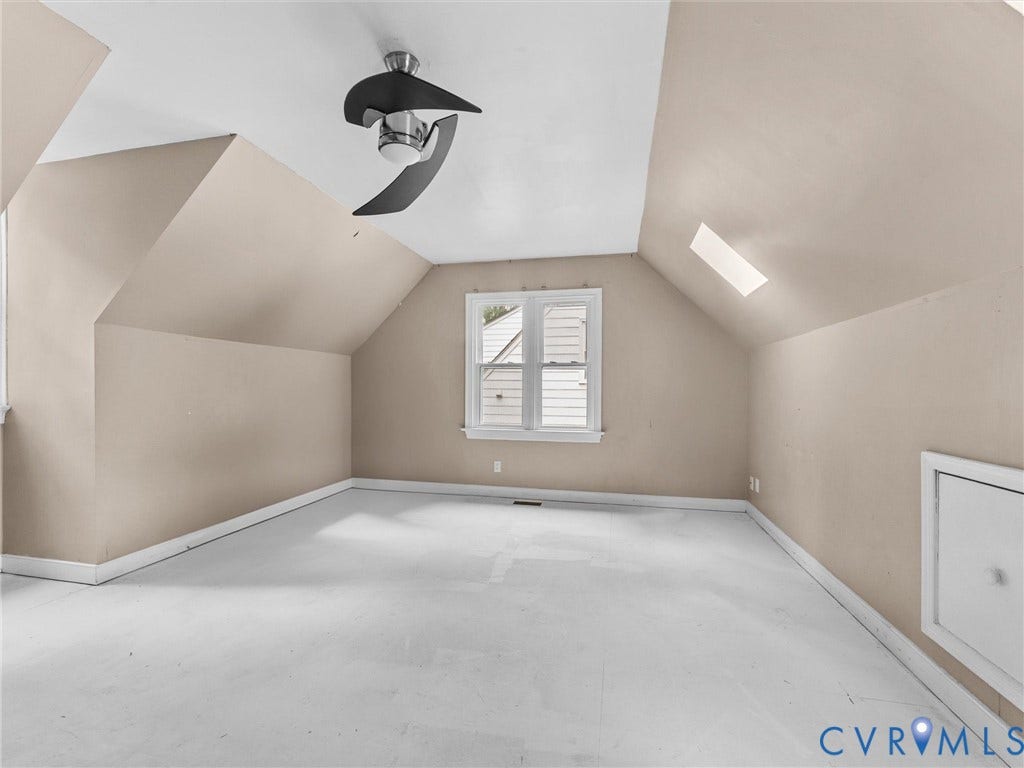 Vaulted ceiling room featuring a skylight, multi-pane window, modern matte black ceiling fan, and access door to built-in attic storage