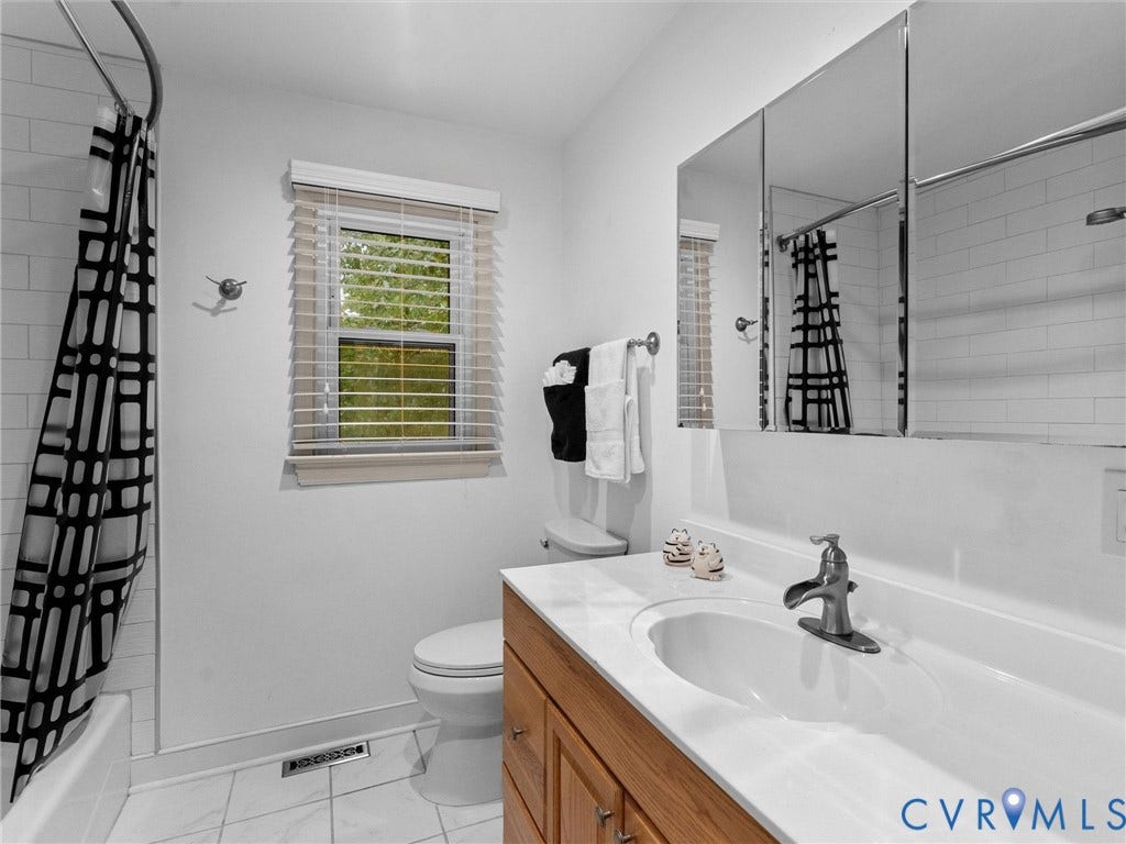 Bathroom featuring a wood-finish vanity, integrated countertop with a white oval basin, three-panel medicine cabinet, tiled tub surround, and tile flooring