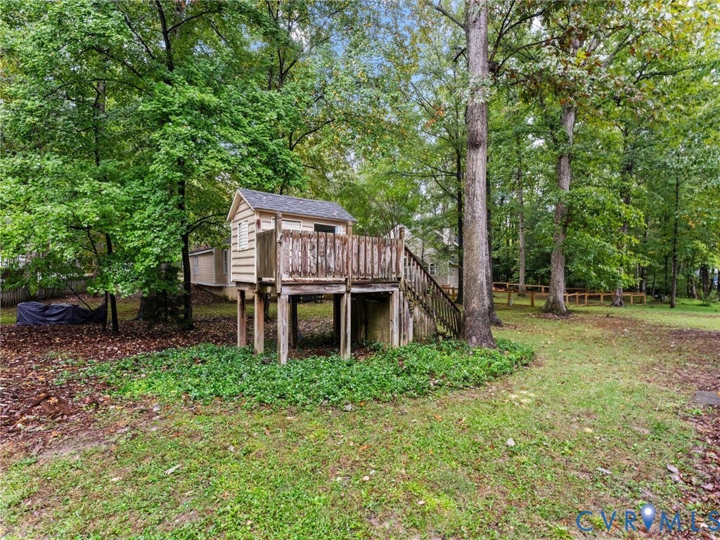 Expansive backyard featuring mature hardwood trees, manicured ground cover, and a raised wooden structure with a built-in staircase and rail system