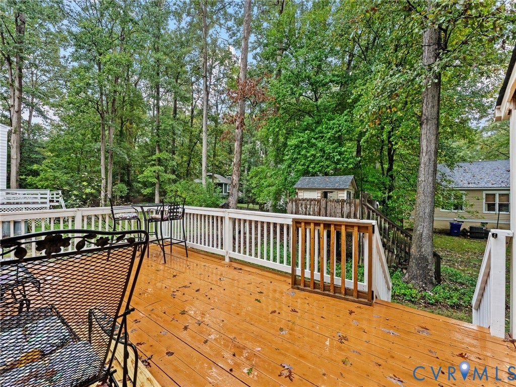 Elevated wood-plank deck featuring white baluster railings and a built-in wooden gate, overlooking a wooded backyard with mature trees