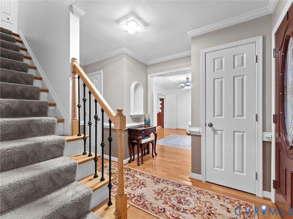Foyer featuring wood-finish flooring, staircase with a wood handrail and black metal balusters, crown molding, arched wall niche, and six-panel interior doors