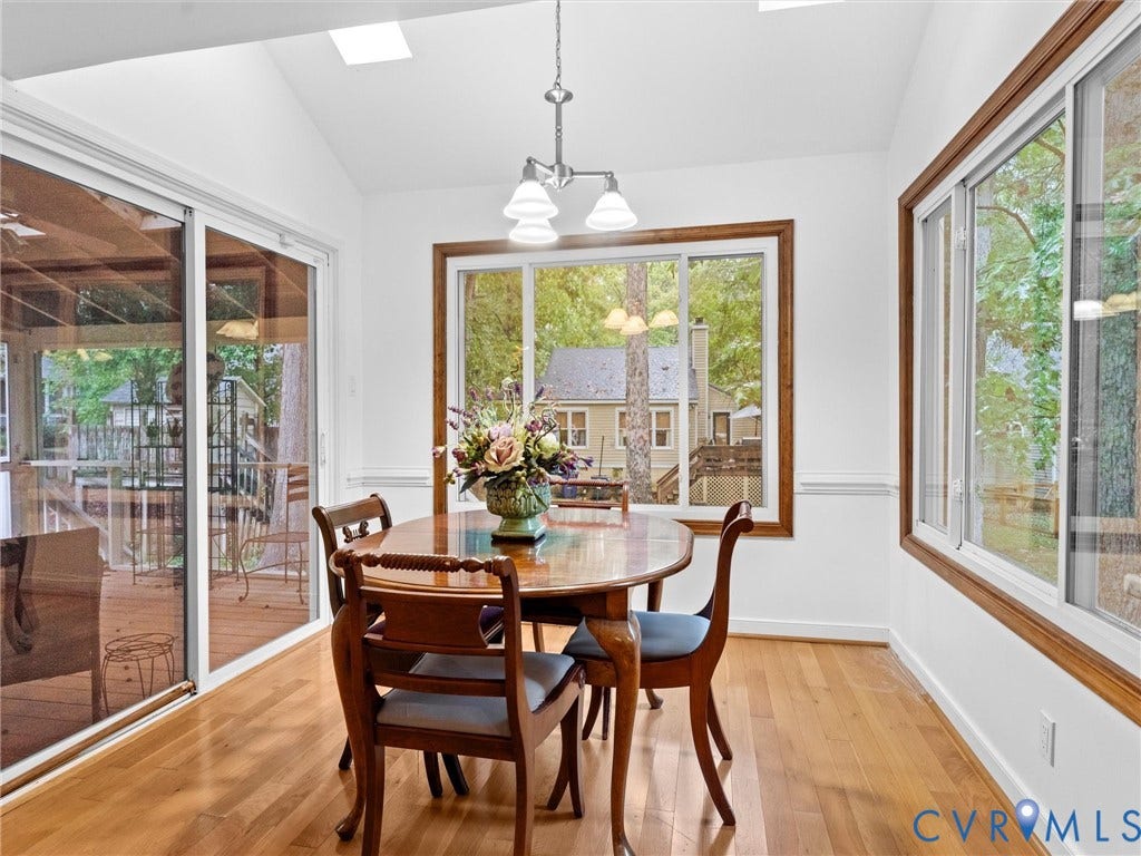 Vaulted ceiling featuring skylights, wood-finish flooring, sliding glass door, and large windows with wood trim