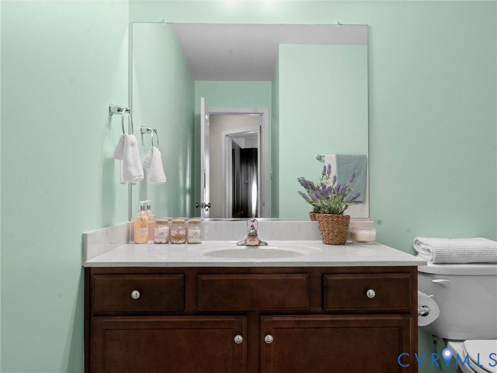 5726 Gossamer Place, Wynwood At FoxCreek, Moseley, VA 23120 Dark wood cabinetry vanity featuring a stone countertop, integrated sink, polished chrome faucet, and a wall-mounted mirror