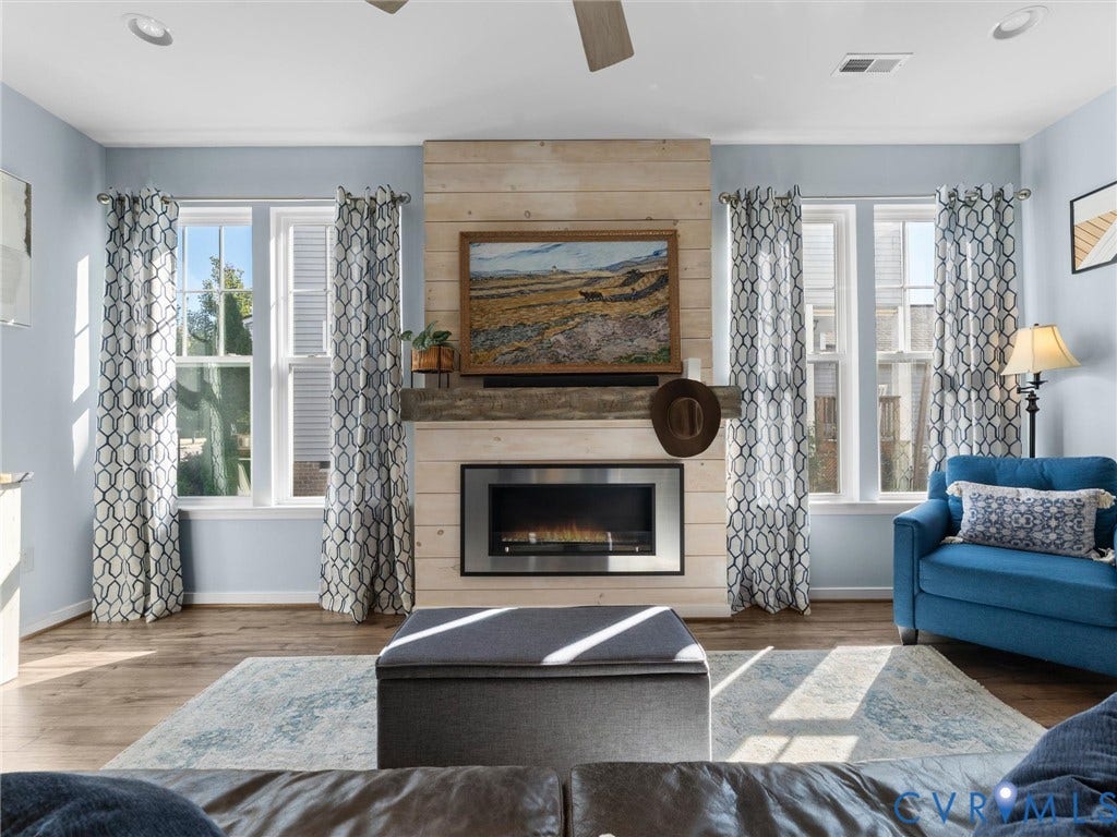 5726 Gossamer Place, Wynwood At FoxCreek, Moseley, VA 23120 Fireplace with a horizontal wood-plank surround and substantial timber mantel, wood-finish flooring, recessed lighting, and multiple tall windows