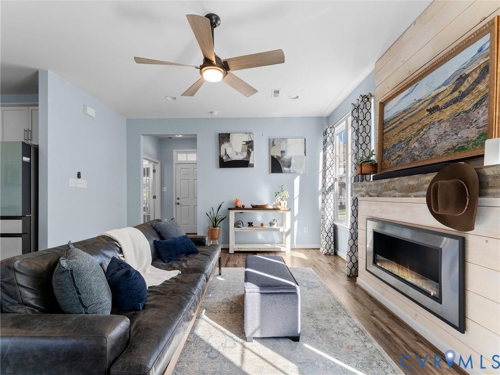 5726 Gossamer Place, Wynwood At FoxCreek, Moseley, VA 23120 Living space featuring horizontal wood-plank wall detailing, a built-in electric fireplace with a stone-texture hearth, wood-finish flooring, and a ceiling fan with integrated lighting