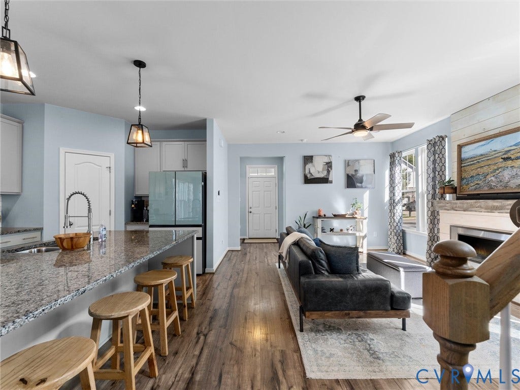 5726 Gossamer Place, Wynwood At FoxCreek, Moseley, VA 23120 Open-concept kitchen featuring an expansive stone-topped island, wood-finish flooring, a fireplace with horizontal shiplap surround, and suspended pendant lighting