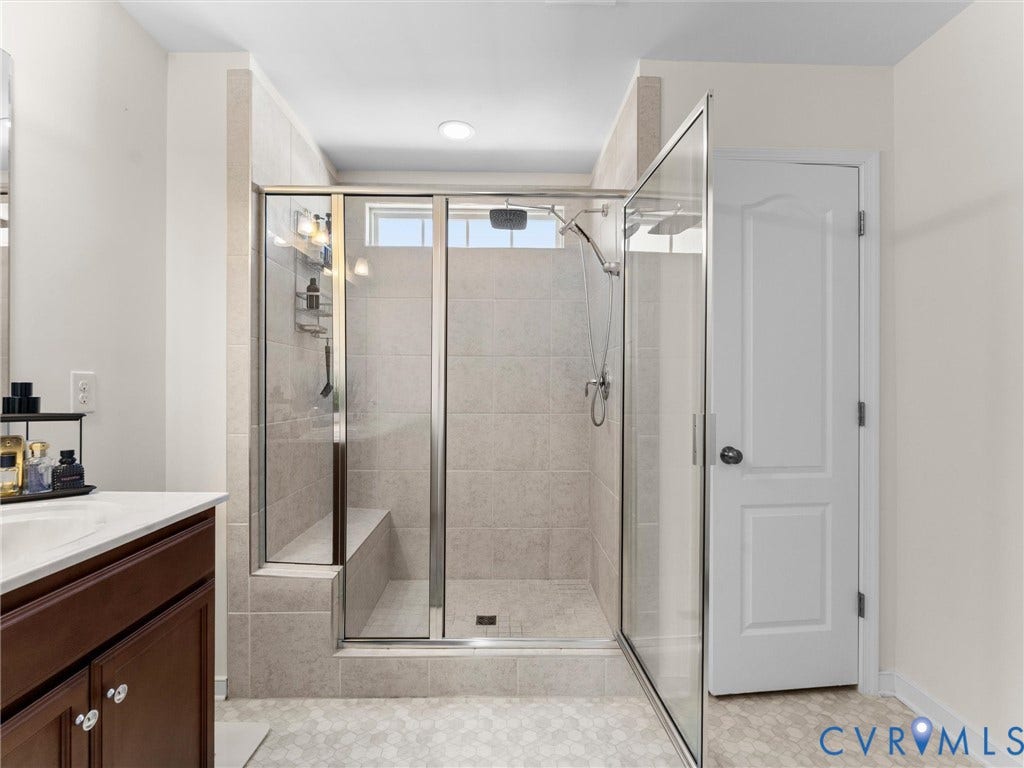 5726 Gossamer Place, Wynwood At FoxCreek, Moseley, VA 23120 Walk-in shower featuring a built-in tiled bench, glass enclosure, and rainfall showerhead, accompanied by a wood-finish vanity cabinet