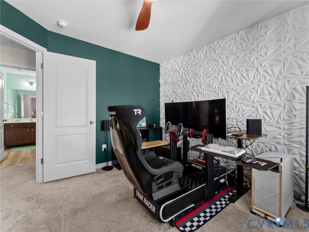 5726 Gossamer Place, Wynwood At FoxCreek, Moseley, VA 23120 Room featuring an accent wall with geometric three-dimensional paneling, deep green painted wall, neutral carpeting, and a ceiling fan with wood-finish blades