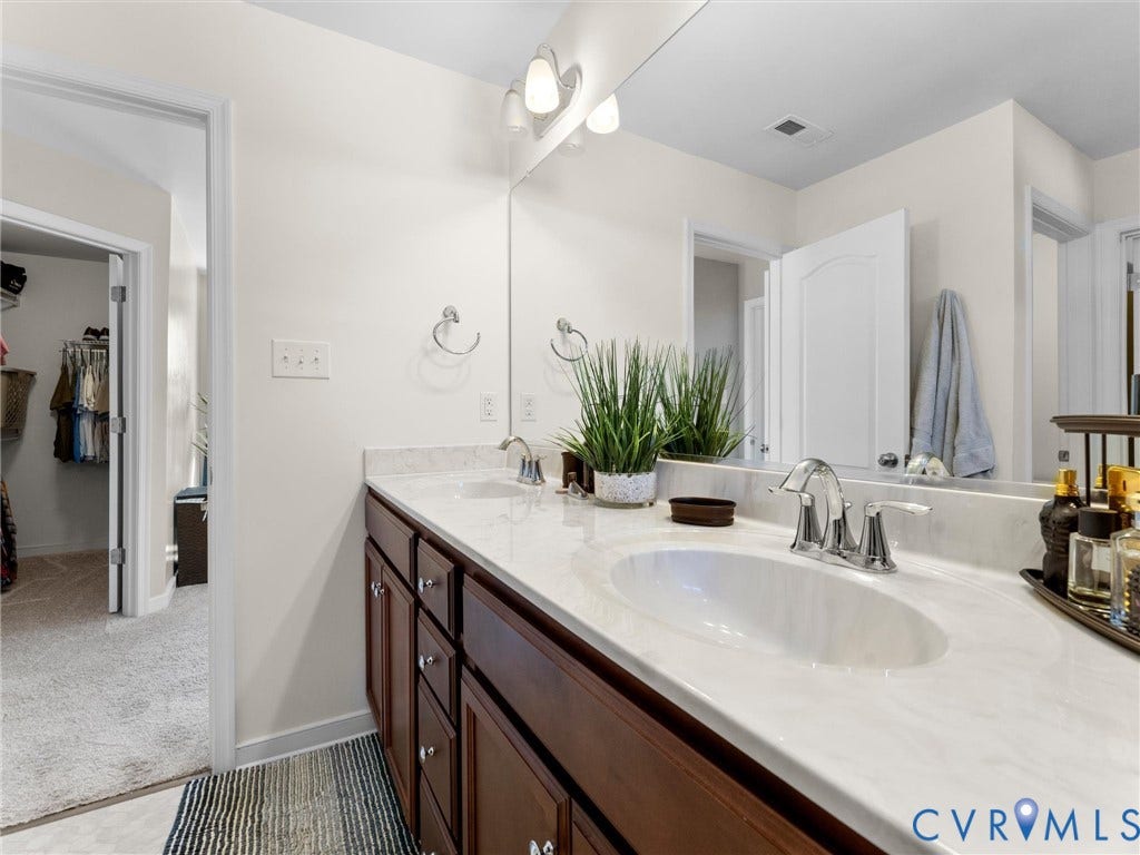 5726 Gossamer Place, Wynwood At FoxCreek, Moseley, VA 23120 Bathroom vanity featuring a light-toned stone-finish countertop, dual under-mount sinks, polished chrome faucets, and stained wood cabinetry