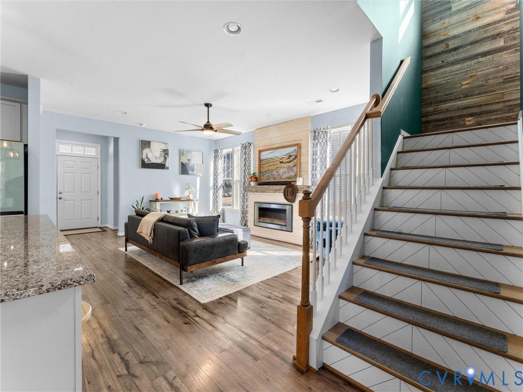 5726 Gossamer Place, Wynwood At FoxCreek, Moseley, VA 23120 Open-concept floor plan featuring wood-finish flooring, staircase with geometric-patterned risers, wood-paneled accent wall, and fireplace with a wood-plank surround