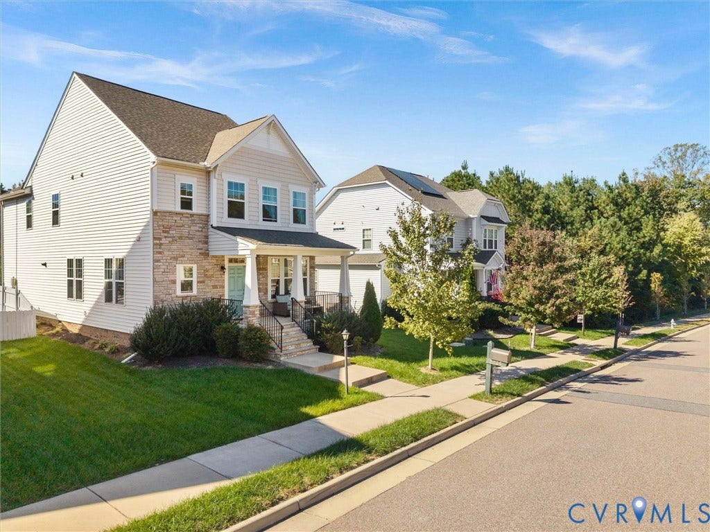 5726 Gossamer Place, Wynwood At FoxCreek, Moseley, VA 23120 Multi-story residence featuring horizontal lap siding, stone veneer facade, covered front porch with iron railing, and roof-mounted solar panels