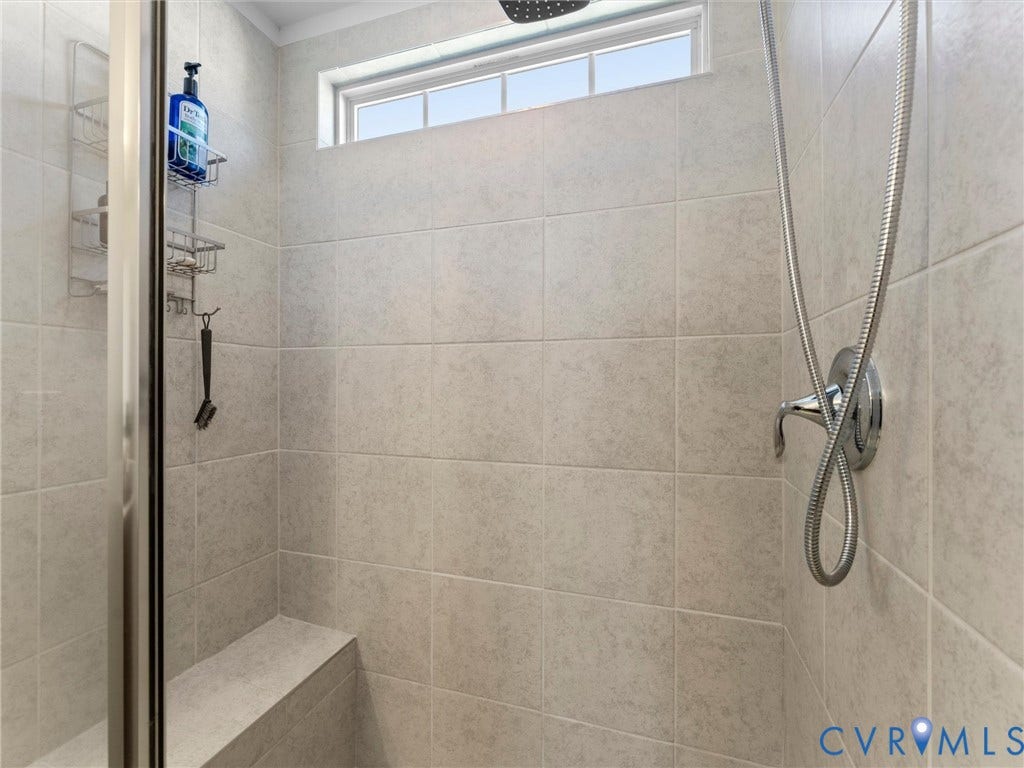 5726 Gossamer Place, Wynwood At FoxCreek, Moseley, VA 23120 Shower enclosure featuring neutral tile wall surrounds, a built-in bench seat, a transom window, and a chrome handheld shower fixture