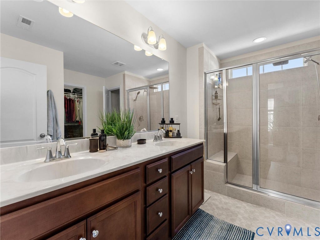 5726 Gossamer Place, Wynwood At FoxCreek, Moseley, VA 23120 Double vanity with a stone countertop, dual undermount sinks, full-width mirror, and a glass-enclosed shower featuring tile surround and a built-in bench
