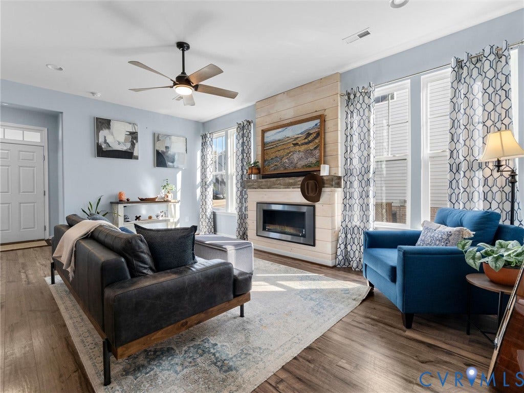 5726 Gossamer Place, Wynwood At FoxCreek, Moseley, VA 23120 Living area featuring wood-finish flooring, a horizontal wood-plank fireplace surround, a metal-framed gas fireplace, and a ceiling-mounted fan with integrated lighting
