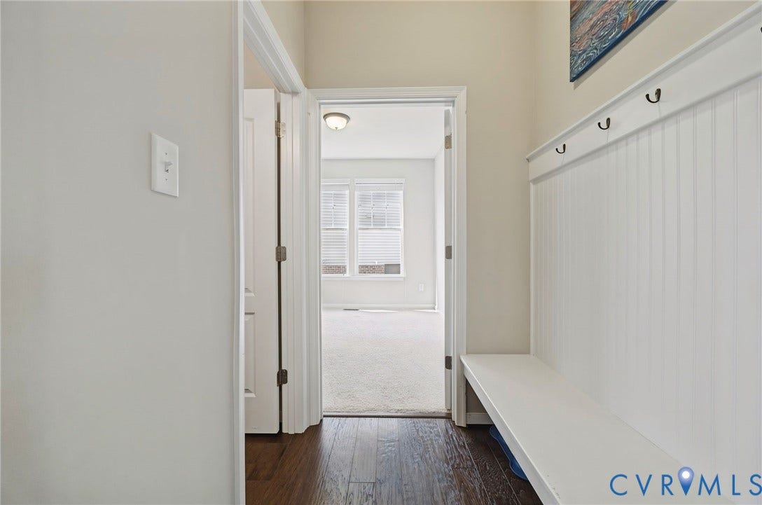 Entryway featuring white beadboard wainscoting, integrated bench seating, wall-mounted hardware hooks, and dark wood-finish flooring