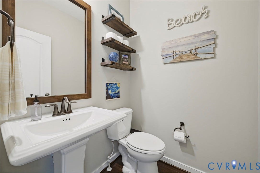 White pedestal sink with a dual-handle metal faucet, framed wood-finish mirror, and three tiered wall-mounted wood-finish shelves