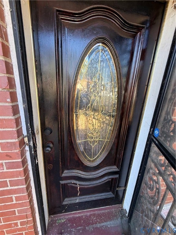 711 Ratcliffe Avenue, Richmond, VA 23222 Dark-stained wood entry door featuring an oval glass insert with decorative caming and multi-paneled millwork, flanked by red brick masonry