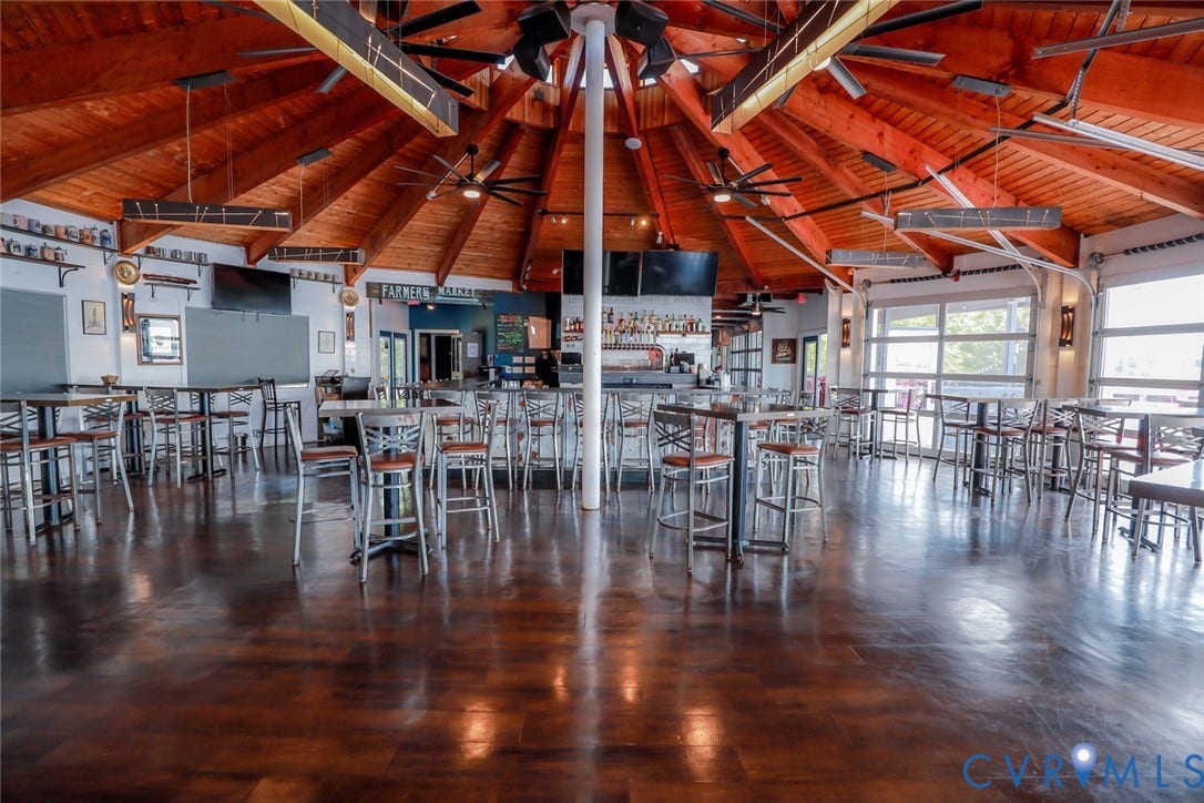 700 Jordan Point Road, North Prince George, VA 23860 Expansive open-concept space featuring a vaulted, radial timber-truss ceiling, stained concrete flooring, multi-panel glass garage-style doors, and a built-in central bar