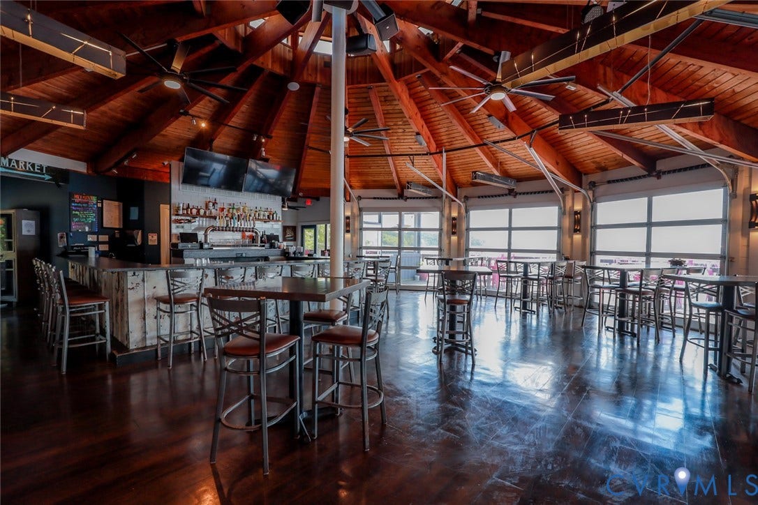 700 Jordan Point Road, North Prince George, VA 23860 Expansive interior featuring an exposed wood-beam conical ceiling, polished wood-finish flooring, a built-in bar with light-toned wood paneling, and multiple glass-paned garage-style doors