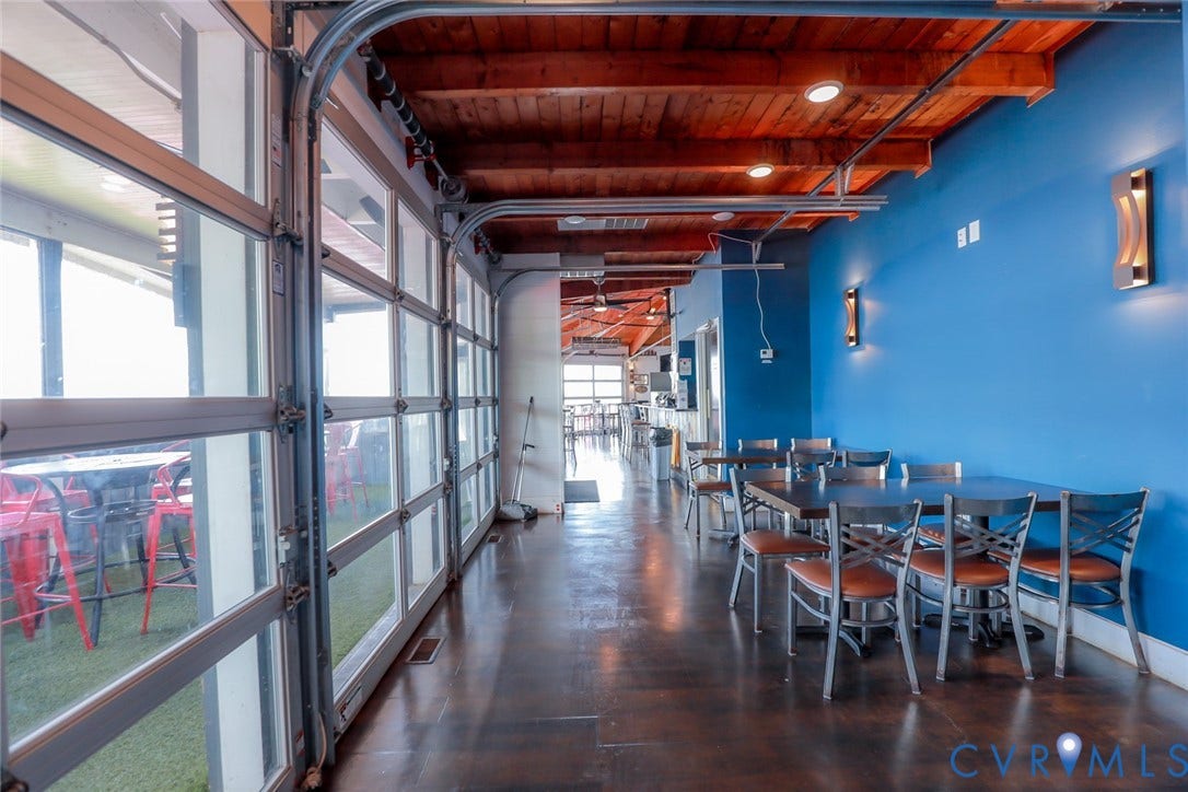 700 Jordan Point Road, North Prince George, VA 23860 Industrial-style space featuring retractable glass garage-style doors, exposed wood-beam ceilings, polished dark flooring, and wall-mounted sconce lighting