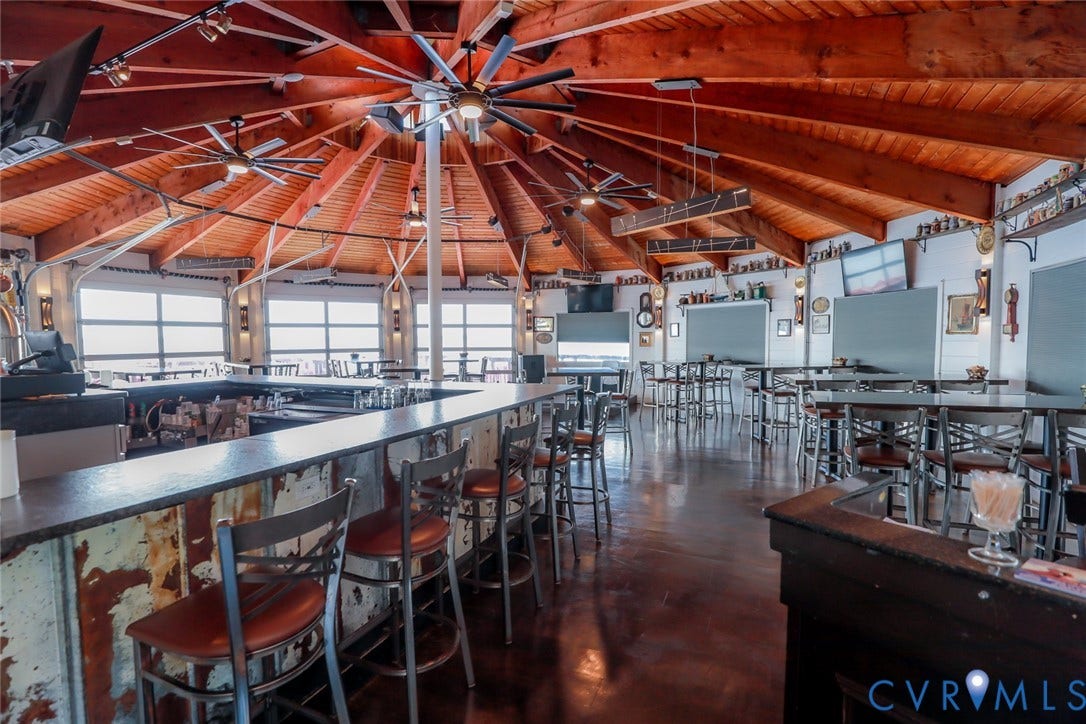700 Jordan Point Road, North Prince George, VA 23860 Expansive vaulted ceiling with exposed natural wood rafters, built-in wrap-around bar with integrated counter, dark polished concrete flooring, and multi-pane window wall